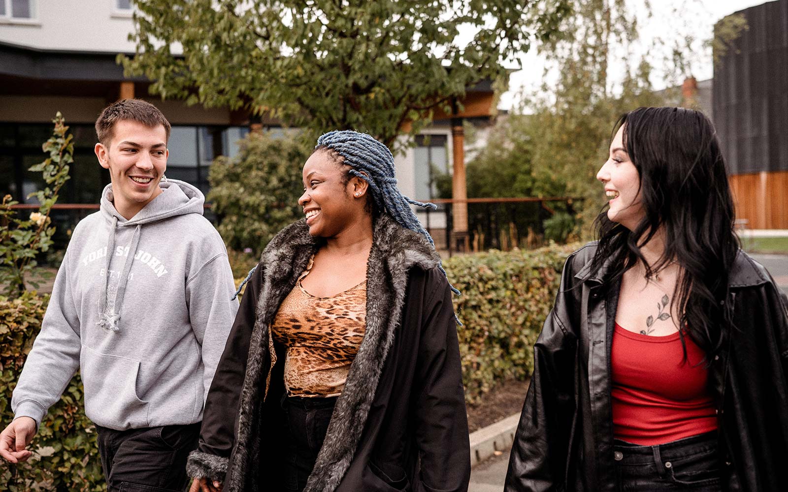 Three students walk across campus, talking and smiling